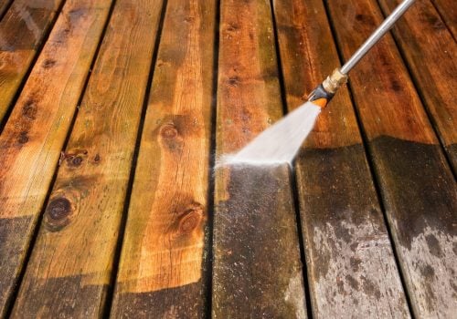 "A pressure washer sprayer is cleaning a weathered treated wood deck. The background area has been cleaned, the lower portion is dirty and weathered, showing the contrast."